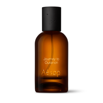 Amber glass Aesop Journey to Ouranon Eau de Parfum bottle with black cap on a white background.