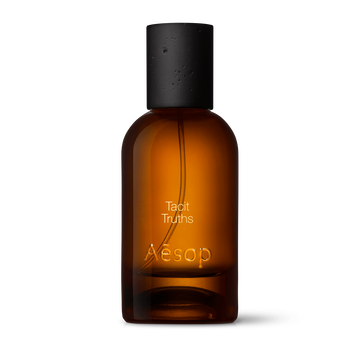 Amber glass Aesop Tacit Truths Eau de Parfum bottle with black cap on a white background.