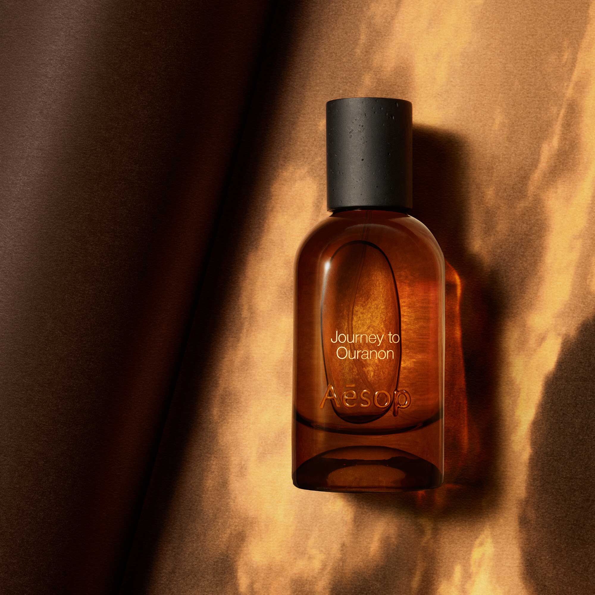 Aesop Journey to Ouranon bottle against a glowing orange draped backdrop.