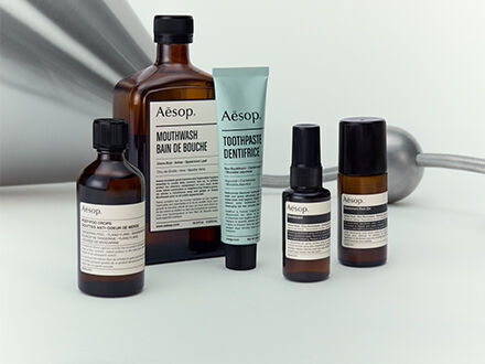 A collection of Aesop personal care products, including mouthwash, toothpaste, and skin treatments, in their signature amber glass bottles and minimalist tubes.
