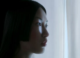 A cinematic, close-up profile of a woman with sleek, dark hair and fair skin, looking thoughtfully toward a source of soft, cool light.