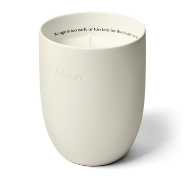 An unlit candle in an off-white rounded vessel, with Aesop embossed outside and a line of text inside the rim.