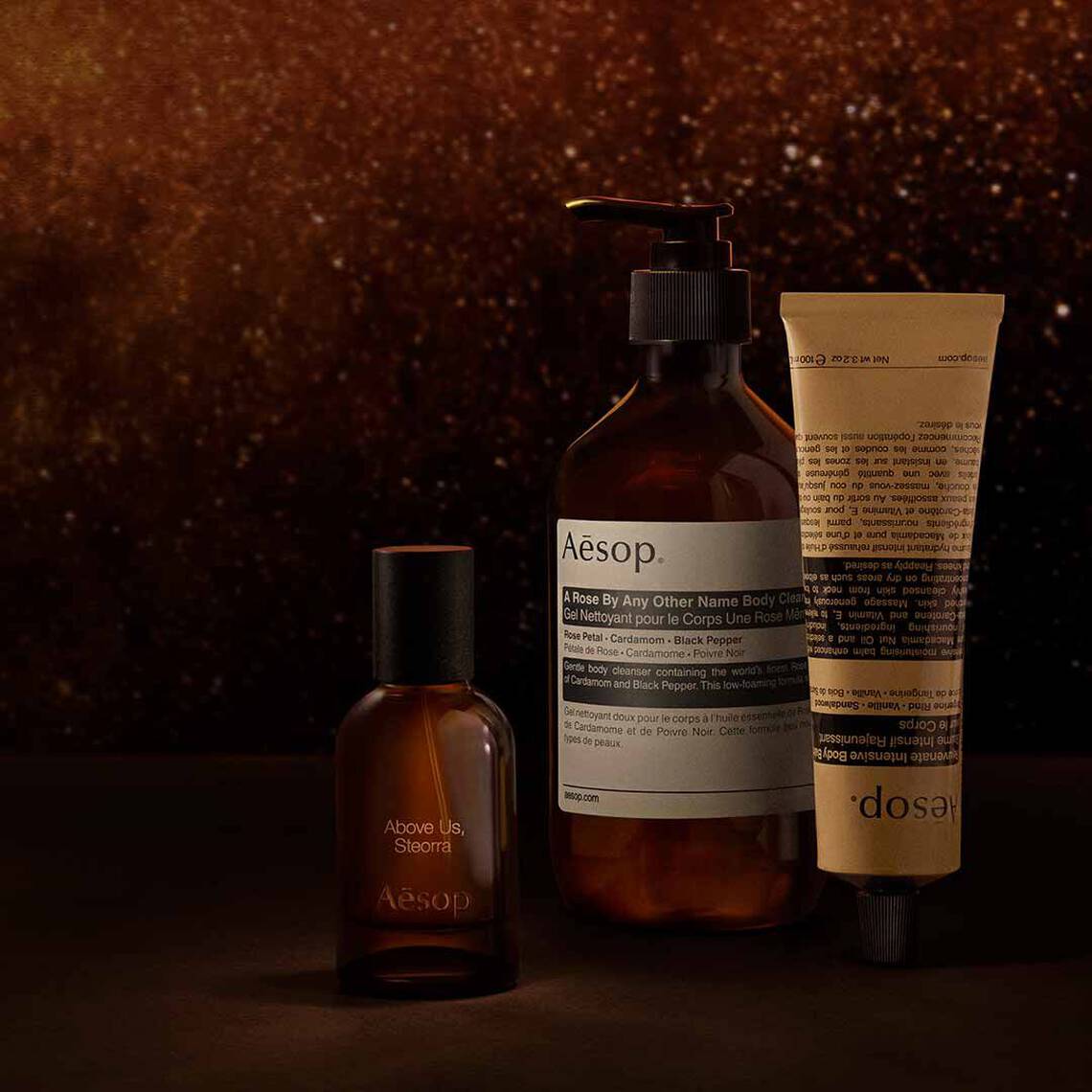 Aesop Above Us, Steorra fragrance bottle, large pump bottle and cosmetic tube arranged on a dark surface.