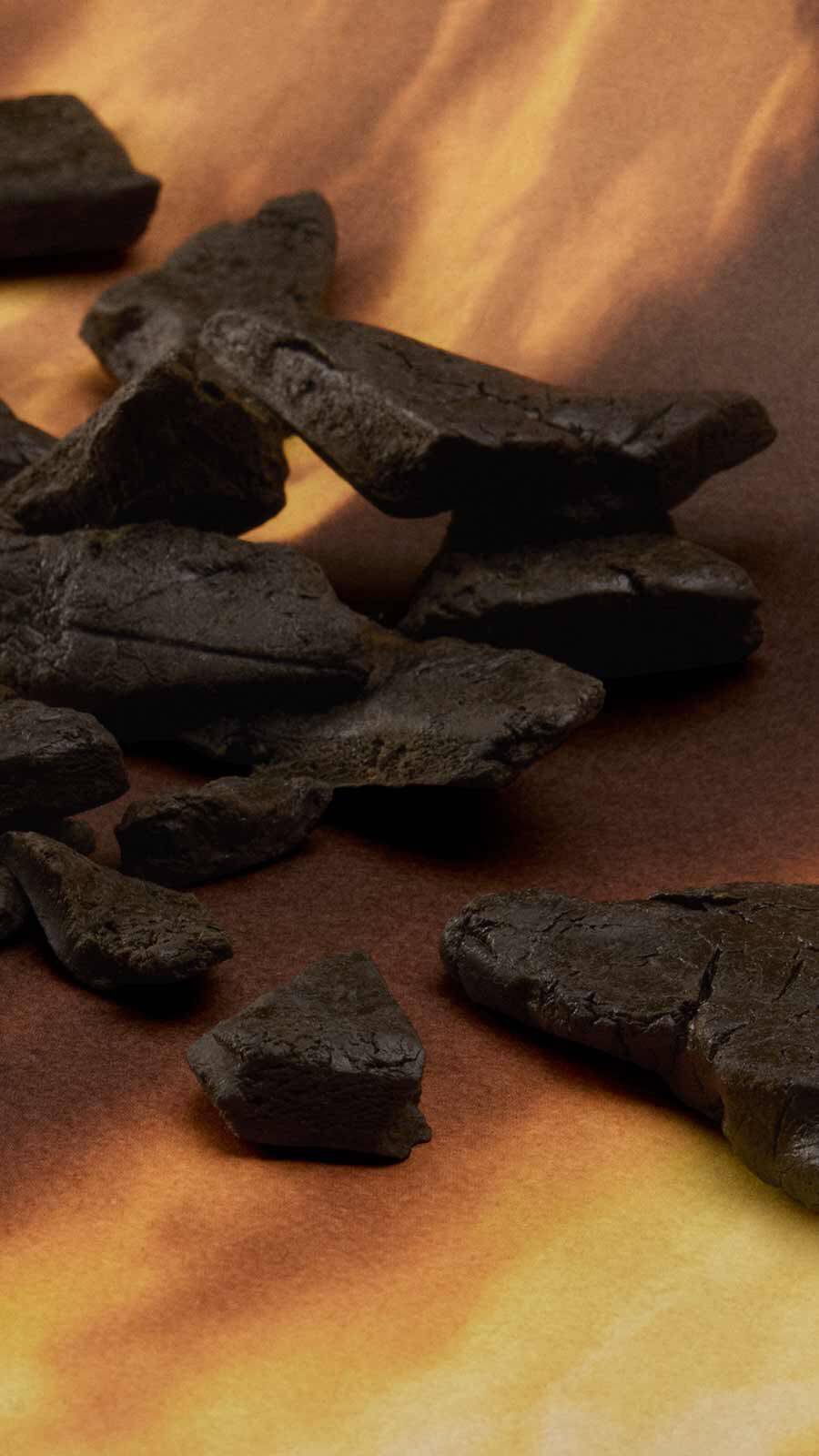 Dark charcoal or oud wood fragments scattered across a warm golden-orange surface.