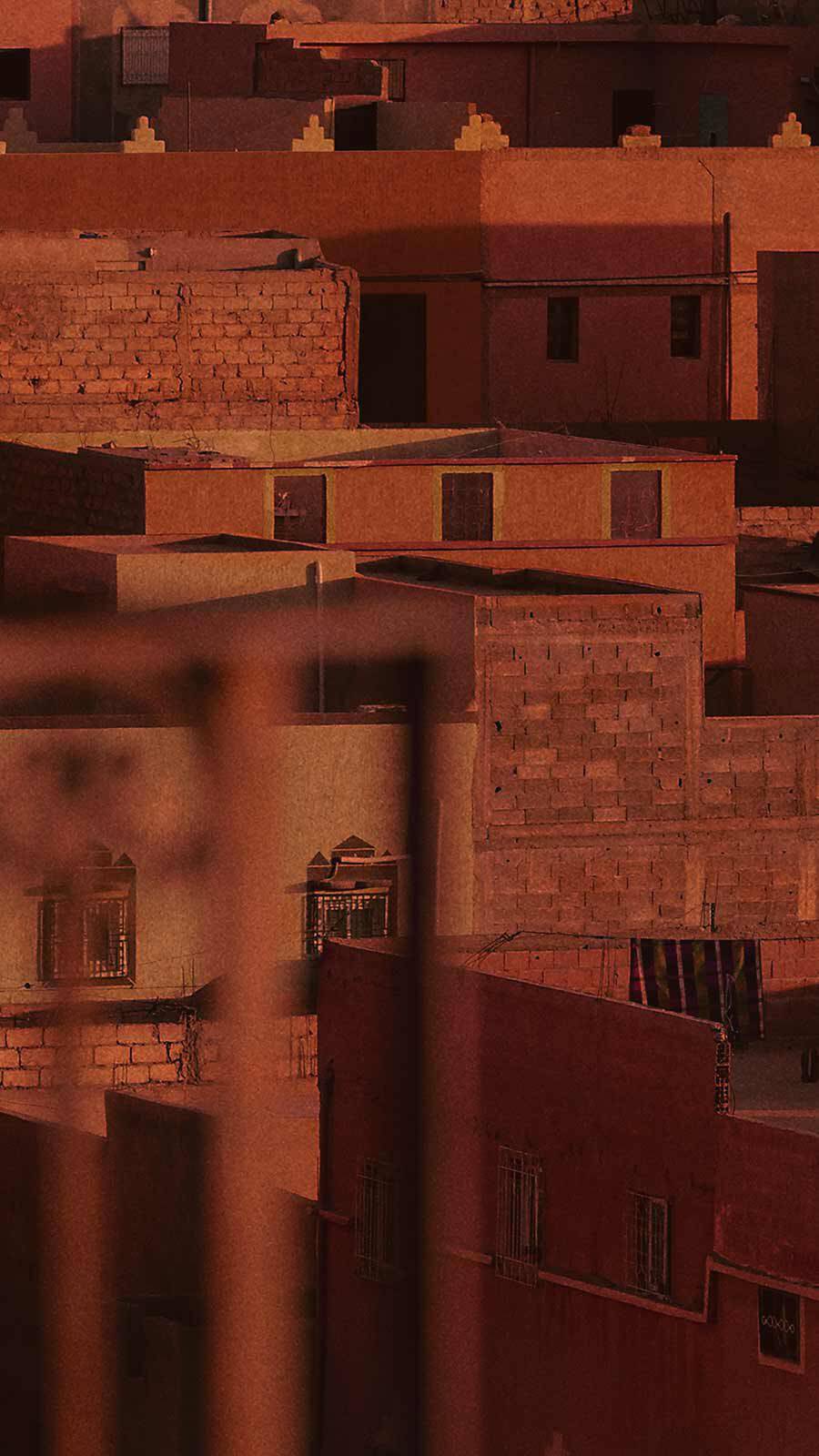 Terracotta-toned Moroccan-style flat-roofed building facades in warm reddish light.