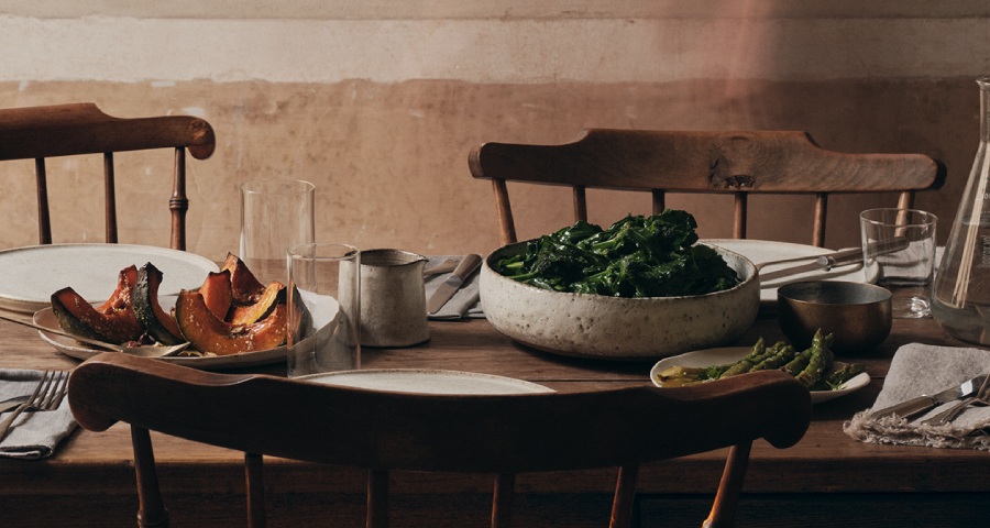 Rustic wooden dining table set with plates, dishes of food, and skincare dropper bottles.