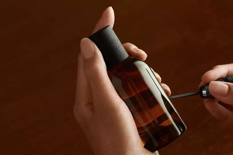 A pair of hands holding an amber glass bottle with a black cap while an engraving tool etches into the surface.