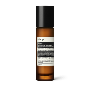 Aesop Solais Replenishing Hand Serum in a slender amber bottle with a tall black cap and cream label on a white background.