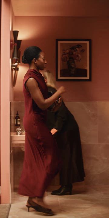 Two people in a softly lit pink-tiled bathroom with a toilet and sink.