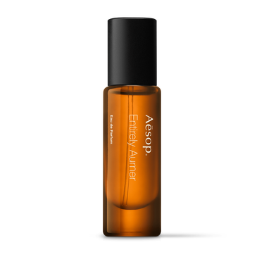 Aesop Entirely Aurner in a slender amber fragrance bottle with white lettering and a tall black cap on a white background.