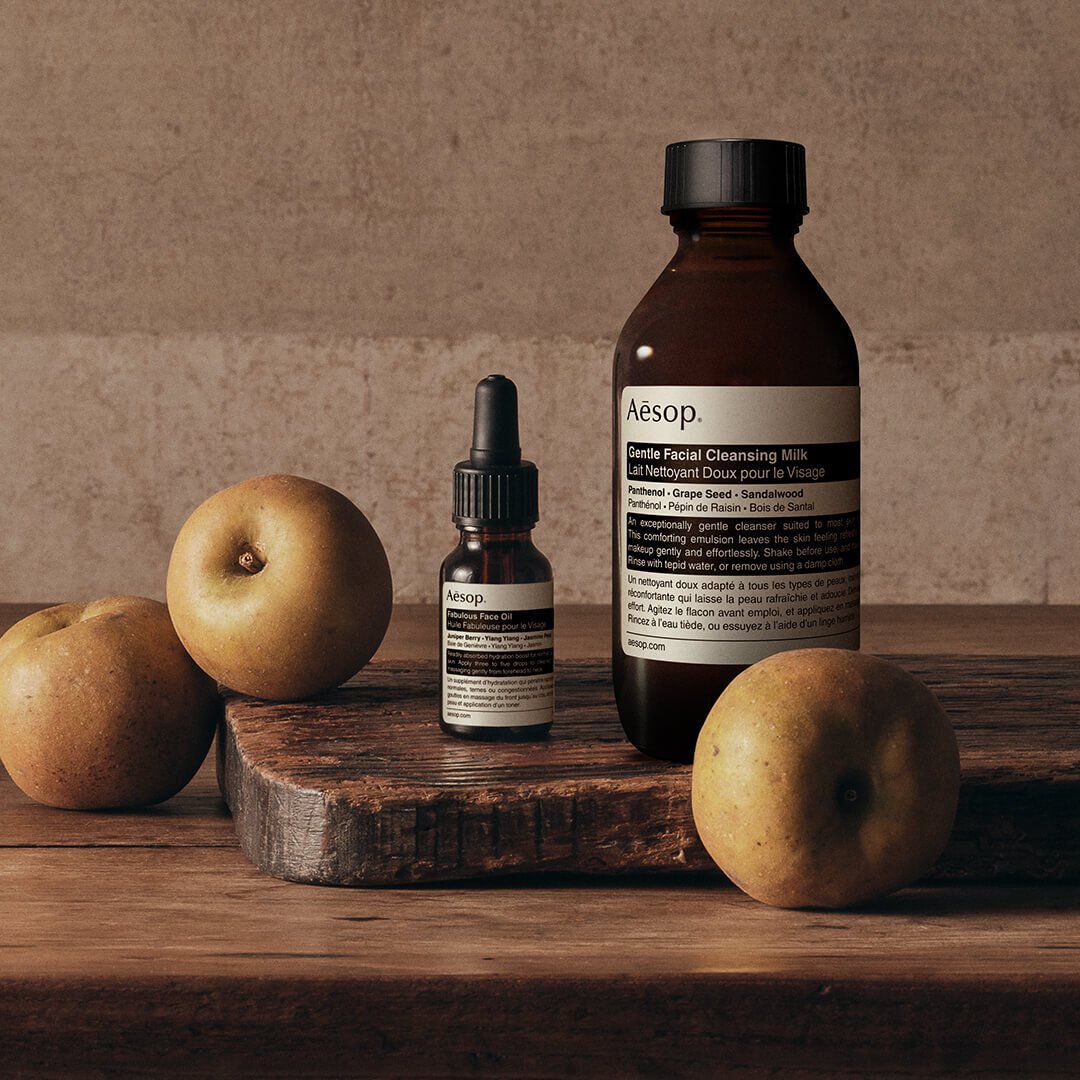Product photography for Aesop featuring Gentle Facial Cleansing Milk and Fabulous Face Oil arranged on a wooden surface with seasonal pears.