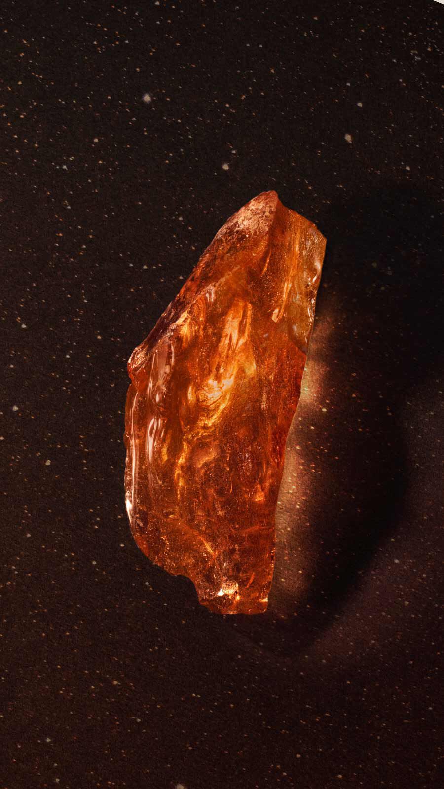 Translucent amber resin fragment with golden shimmer against a dark background with fine sparkles.