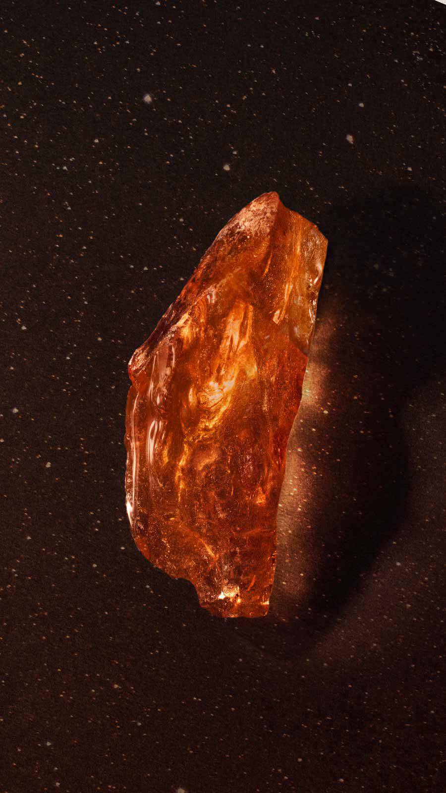Translucent amber resin fragment with golden shimmer against a dark background with fine sparkles.