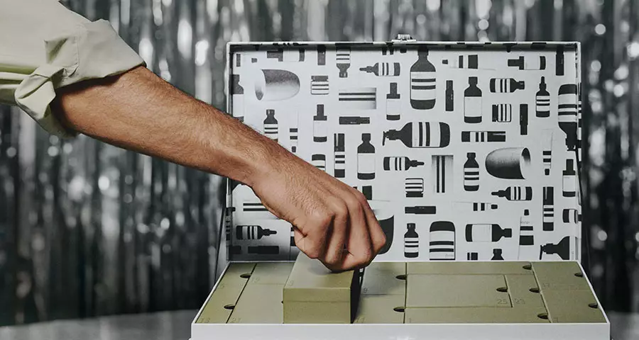 A hand lifts a numbered drawer from an open festive gift box, with a monochrome product-pattern backdrop.