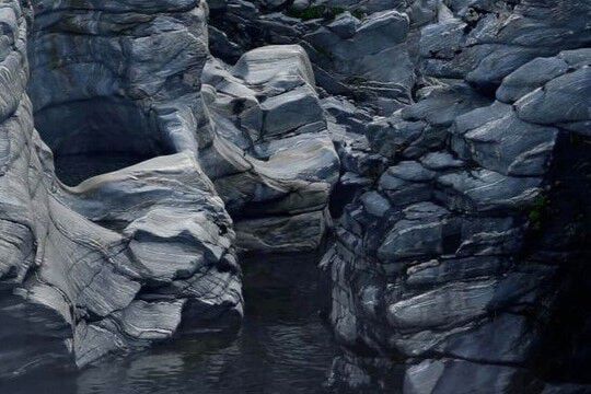 Dark blue-grey rocky gorge with layered sculpted stone formations and a still dark water pool.
