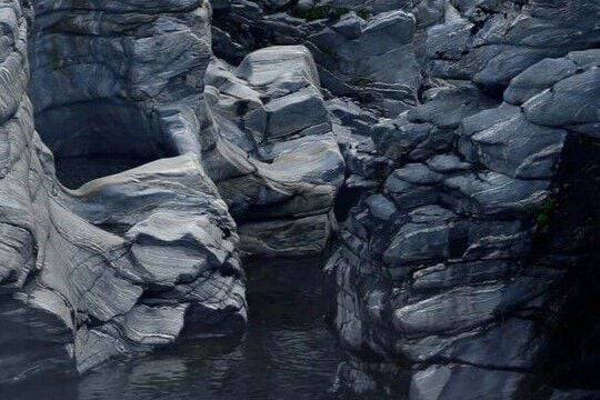 Dark blue-grey rocky gorge with layered sculpted stone formations and a still dark water pool.