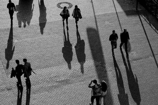 Black and white image with people walking on the streets reflecting shadows.