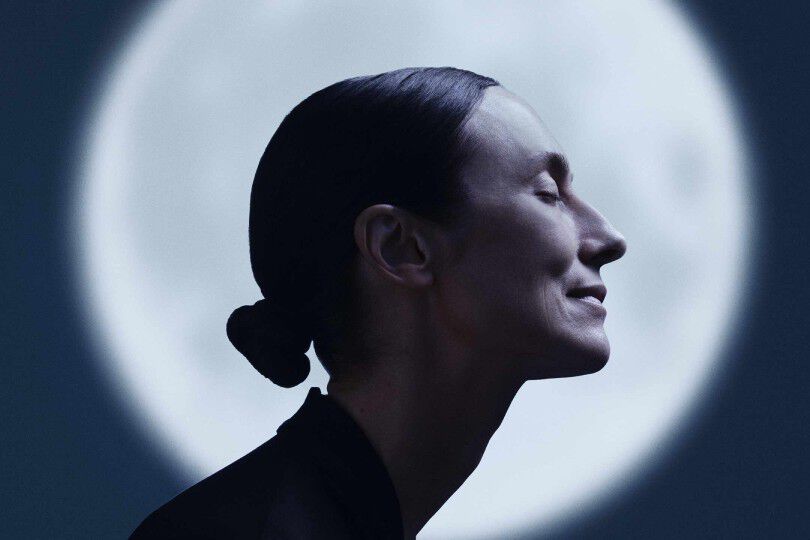 Profile of a person with sleek hair in a low bun, lit against a circular spotlight.