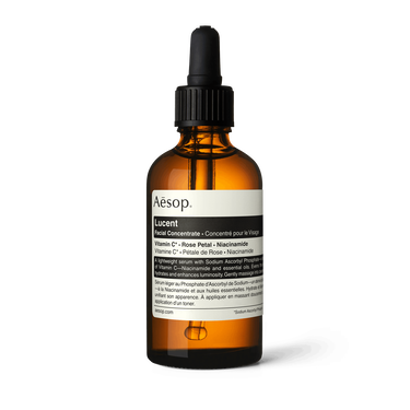 Aesop Lucent Facial Concentrate in an amber bottle with a black pipette cap and cream label on a white background.