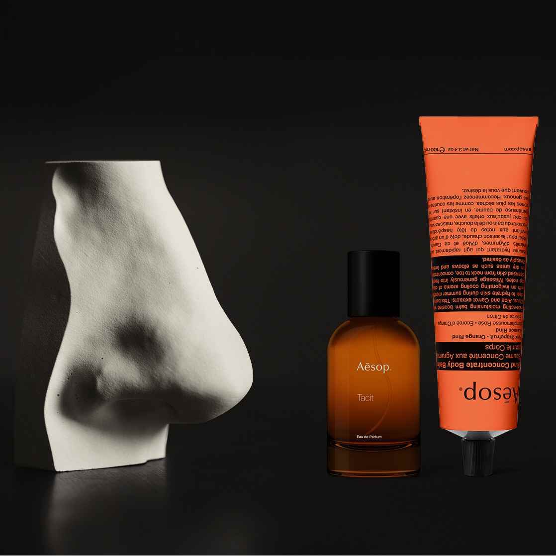 A sculptural white nose reflected in a round mirror, with Aesop perfume and hand cream in the foreground.