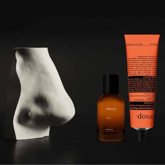 A sculptural white nose reflected in a round mirror, with Aesop perfume and hand cream in the foreground.