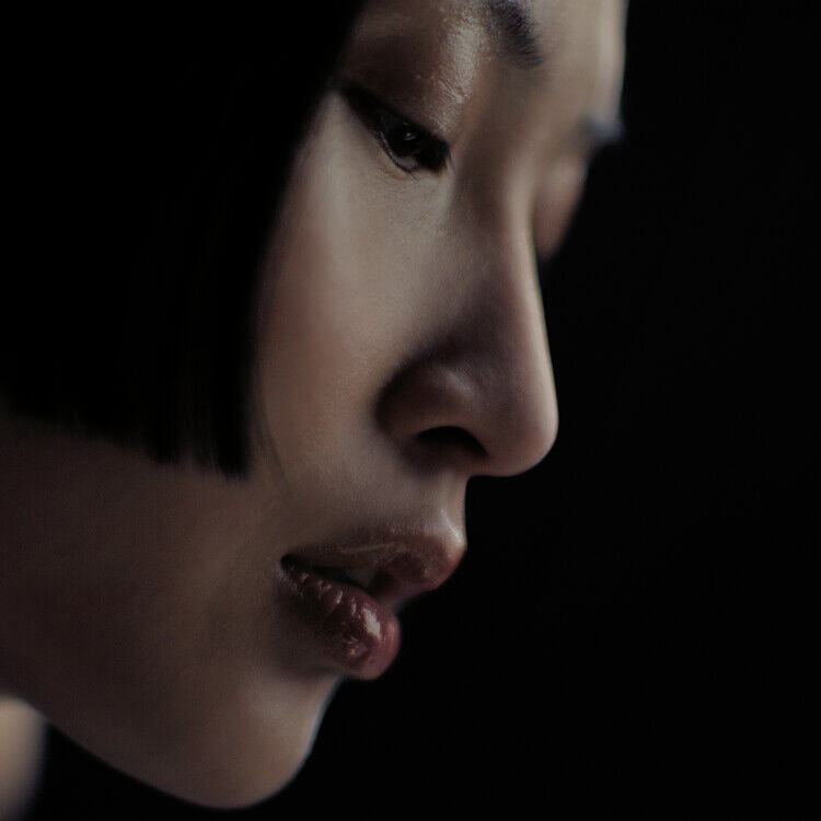 Moody close-up profile of a person with a short dark bob in low-key lighting.