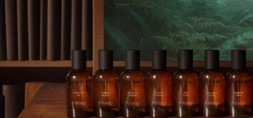 A lineup of amber glass Aesop perfume bottles displayed on a wooden shelf.