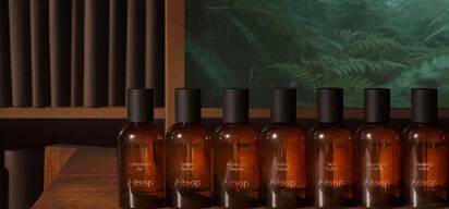 A lineup of amber glass Aesop perfume bottles displayed on a wooden shelf.