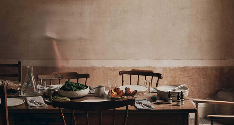 Rustic wooden dining table set with plates, dishes of food, and skincare dropper bottles.