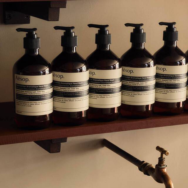 Row of amber Aesop hand wash bottles on a dark wooden shelf above a brass tap.