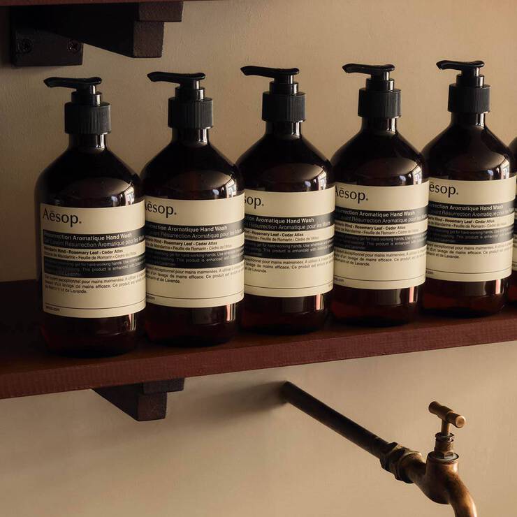 Row of amber Aesop hand wash bottles on a dark wooden shelf above a brass tap.